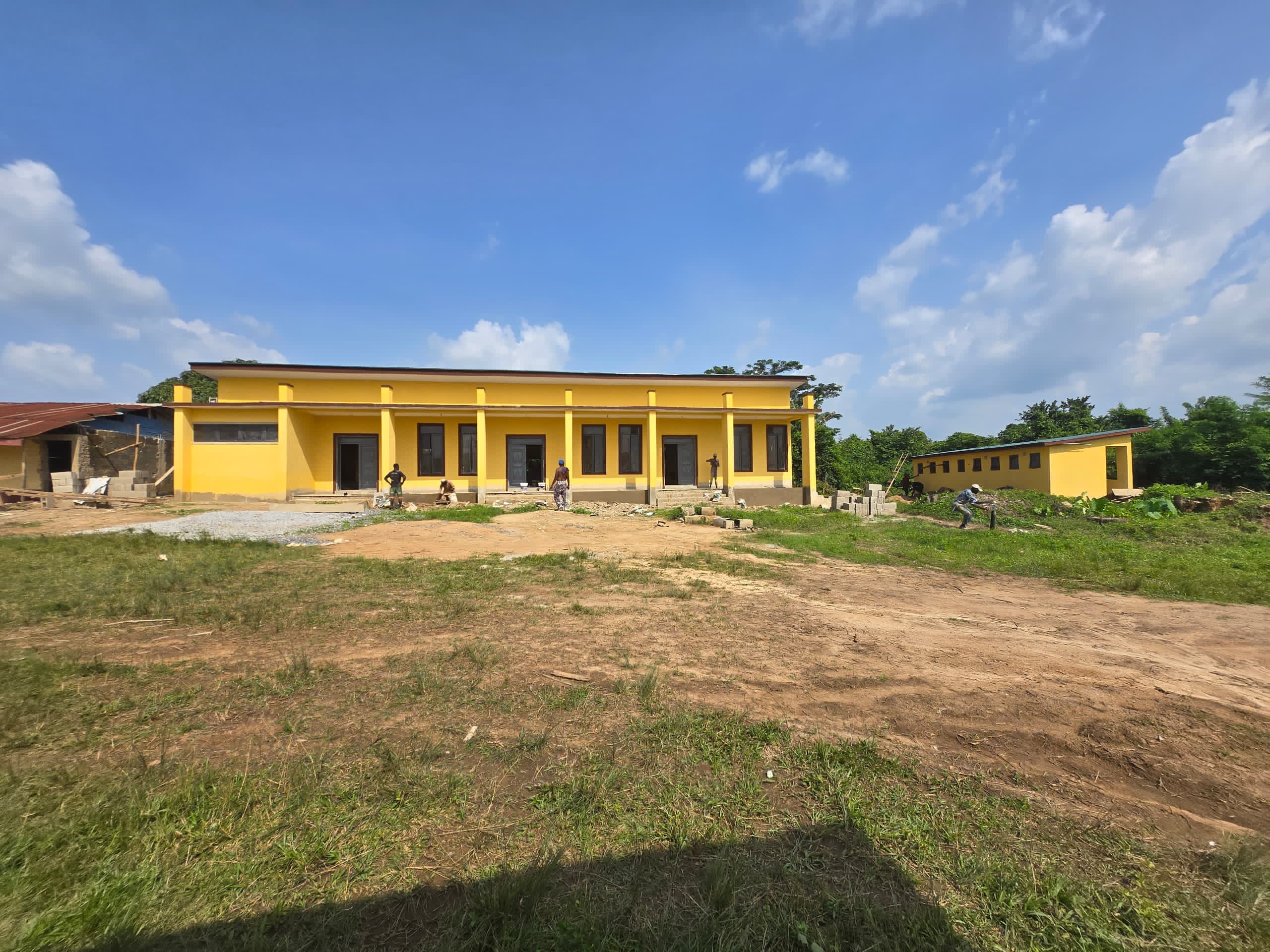 Secondary school hall block under construction &mdash; yellow render, workers visible